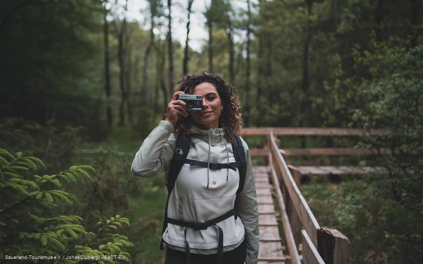 Eine Frau steht mit dem Fotoapperat auf einem Steg in den Ebbemooren