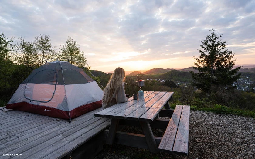 Eine Frau genießt den Sonnenaufgang am Trekkingplatz Talblick