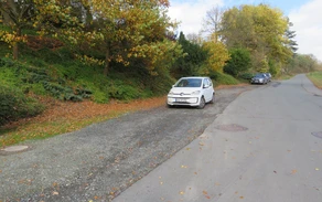 Ein Schotterparkplatz neben einer Straße mit drei parkenden Autos.